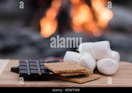 Smores Zutaten an einem Strand mit Lagerfeuer mit Schokolade, Eibisch, und Graham Cracker mit Raum für Kopie Stockfoto