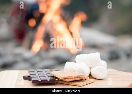 Smores Zutaten an einem Strand mit Lagerfeuer mit Schokolade, Eibisch, und Graham Cracker mit Raum für Kopie Stockfoto