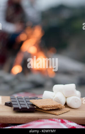 Smores Zutaten an einem Strand mit Lagerfeuer mit Schokolade, Eibisch, und Graham Cracker mit Raum für Kopie Stockfoto