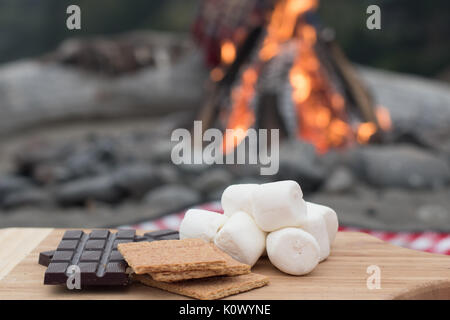 Smores Zutaten an einem Strand mit Lagerfeuer mit Schokolade, Eibisch, und Graham Cracker mit Raum für Kopie Stockfoto