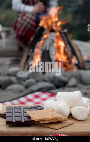 Smores Zutaten an einem Strand mit Lagerfeuer mit Schokolade, Eibisch, und Graham Cracker mit Raum für Kopie Stockfoto