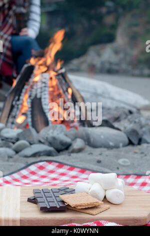 Smores Zutaten an einem Strand mit Lagerfeuer mit Schokolade, Eibisch, und Graham Cracker mit Raum für Kopie Stockfoto