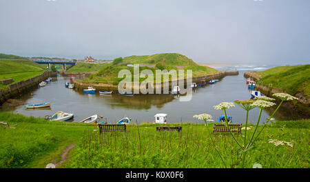 Boote im geschützten Hafen von Seaton Sluice in der Nähe von Dorf an der Küste von Hartley, mit Road Bridge, Stadt, & Sandstrand in der Nähe, England Stockfoto