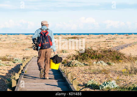 Meer Fischer oder Angler zu Fuß entlang der Promenade über Kies zum Strand von Dungeness in Kent. Stockfoto