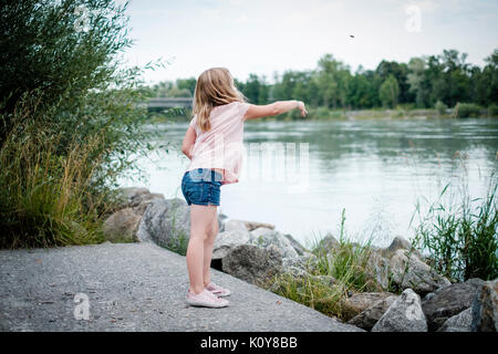 Kleines Mädchen mit Steinen werfen in einen Fluss Stockfoto