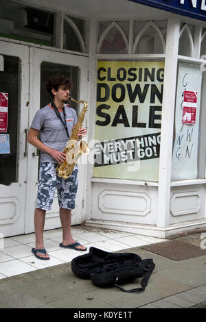 West Wales. Haverford West. Bridge Street. Gaukler spielen ein Saxophon außerhalb einer geschlossen Shop. Stockfoto