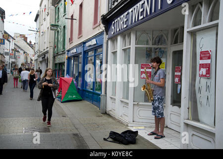 West Wales. Haverford West. Bridge Street. Gaukler spielen ein Saxophon außerhalb einer geschlossen Shop. Stockfoto