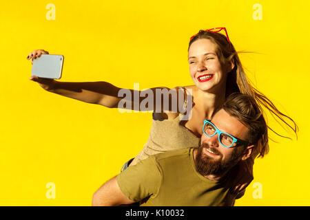 Glück Paar. Piggyback. Selfie. Hipster Paar macking selfie auf gelben Hintergrund. Studio shot Stockfoto