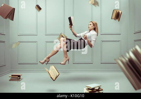 Eine entspannte Frau levitates in einem Raum voller Fliegen Bücher Stockfoto