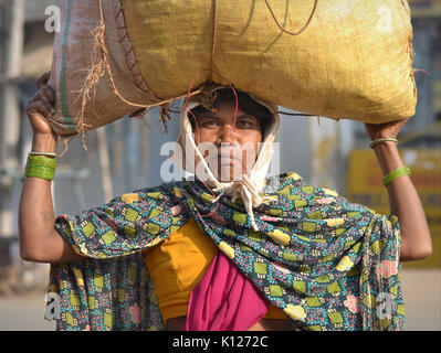 Die indische Adivasi-Frau (Stammfrau) mit zwei markanten goldenen Nasenstollen trägt auf dem Kopf eine Tüte Gemüse und Posen für die Kamera. Stockfoto