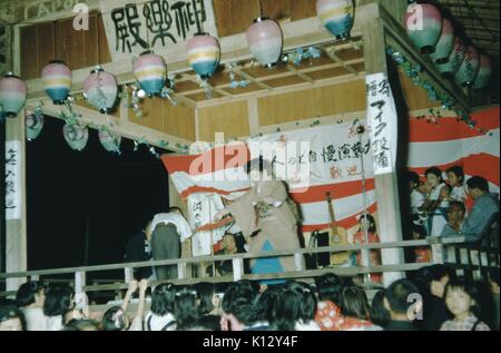 Japanische Frau auf der Bühne in einem Kabuki Theater Produktion, ausgestreckten Armen und deutete auf eine Menge, einer jungen männlichen Schauspieler mit auf der Bühne, Papier Laternen rund um die Bühne, 1952. Stockfoto