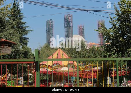 Städtische Szene in Tirana, Albanien. Fun Park mit Nostalgie Kinder Karussell hinter einem Zaun, hinter der Großen Moschee im Bau. Im Süden Europas. Stockfoto