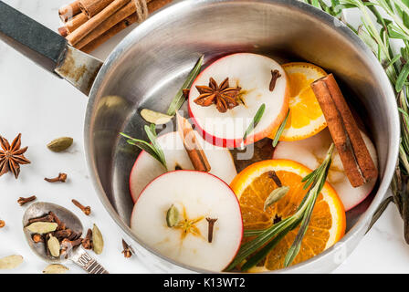 Traditionelle Winter und Weihnachten Getränke, Zutaten für Glühwein, heiße Getränke mit Zitrusfrüchten, Apple und Gewürze in Aluminium Kasserolle auf weißem Marmor t Stockfoto