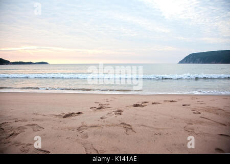 Wellen auf einen Strand unter einem pinkfarbenen und blauen Himmel in Cape Breton, Nova Scotia Stockfoto