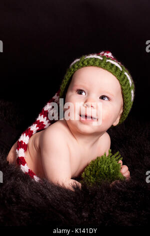 Portrait von lächelnden Mädchen tragen ungewöhnliche lange grüne und weiße und rote Strickmütze, dunklen Hintergrund Stockfoto