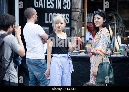 London, Großbritannien - 17. August 2017: Columbia Road Flower Sonntag Markt. Zwei Mädchen posieren mit einem Cocktail in der Hand Stockfoto