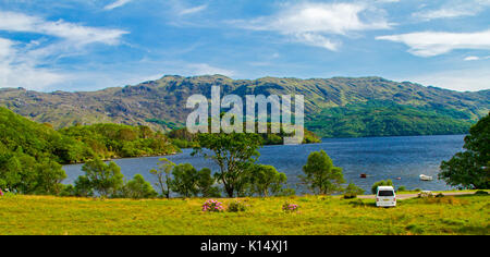 Atemberaubende Landschaft mit Loch Morar mit zerklüfteten Bergen und Wohnmobil im Abstand neben ruhigen blauen Wasser unter blauem Himmel in Schottland gesäumt Stockfoto