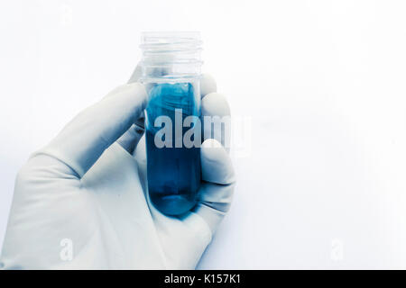 Hand mit Latex Handschuhe halten ein Glas Prüflabor Rohr mit blauer Flüssigkeit und blauen Tönen, auf weißem Hintergrund Stockfoto