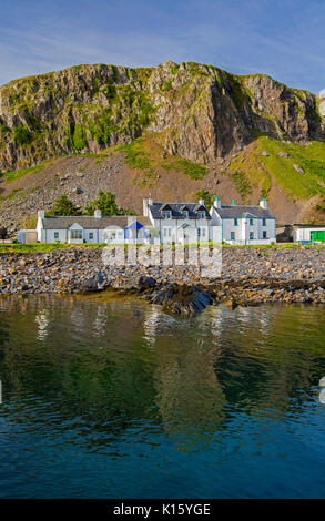Herrliche Aussicht auf Dorf, Seil Ellenabeich/Easdale Island, Schottland, mit weißen Häuschen an der Basis der felsigen Klippen in ruhigen Gewässern des Ozeans reflektiert Stockfoto