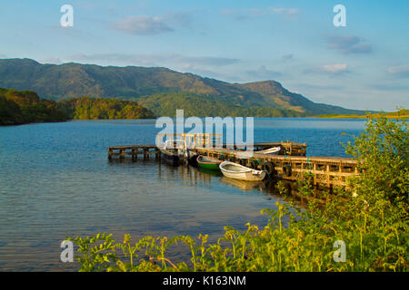 Ruhige, blaue Wasser des Loch Morar gesäumt mit zerklüfteten Bergen und mit Booten an der alten Holzsteg unter blauem Himmel Schottland günstig Stockfoto