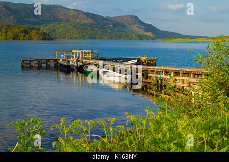 Ruhige, blaue Wasser des Loch Morar gesäumt mit zerklüfteten Bergen und mit Booten an der alten Holzsteg unter blauem Himmel Schottland günstig Stockfoto