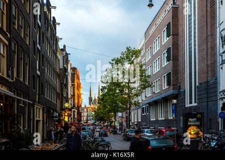 Am frühen Abend, wenn die Sonne untergeht, im historischen Zentrum von Amsterdam mit einer großen Kirche mit Türmen im Hintergrund Stockfoto