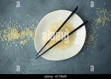 Porzellanteller und Reis auf grauem Beton Tabelle mit Copyspace Stockfoto