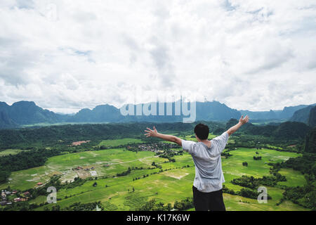 Ein Mann die Hand heben auf der Bergspitze, in tropischen Landschaft reisen, Vang Vieng in Laos. Stockfoto