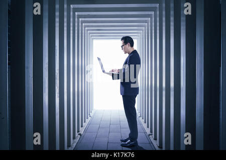 Geschäftsmann mit Laptop mit Line-förmige Korridore Hintergrund zu erhalten, auf Nacht, Szene. Stockfoto