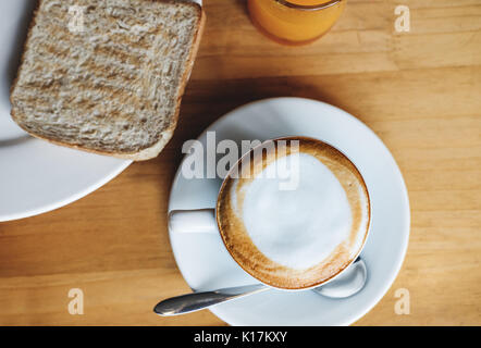 Morgen heißen Cappuccino mit Geröstetes Vollkornbrot und Orangensaft, auf hölzernen Tisch Stockfoto