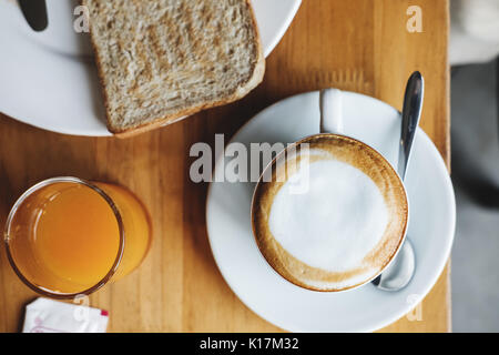 Morgen heißen Cappuccino mit Geröstetes Vollkornbrot und Orangensaft, auf hölzernen Tisch Stockfoto