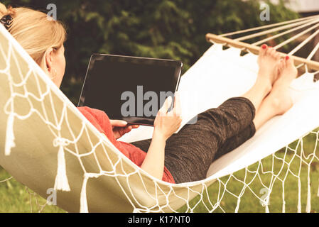 Schöne Frau entspannen auf einer Hängematte mit und Verwendung digitaler Tablet (Vintage Effekt). Stockfoto