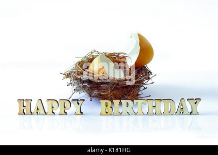 Isolierte zerbrochene Eierschale auf einem Nest mit Holz Alphabete für Happy Birthday Konzept Stockfoto