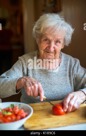 Eine ältere Frau Koteletts Tomaten für einen Salat. Stockfoto