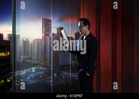 Junge asiatische Geschäftsmann Holding und Verwendung digitaler Tablet. Abend Szene. Stockfoto