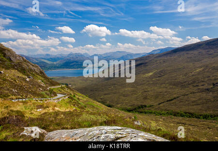 Kurvenreiche Straße durch baumlose Hügel zum Meer Meerenge an Kylereah, Isle of Skye, mit Bergen über Wasser unter blauem Himmel in Schottland Stockfoto