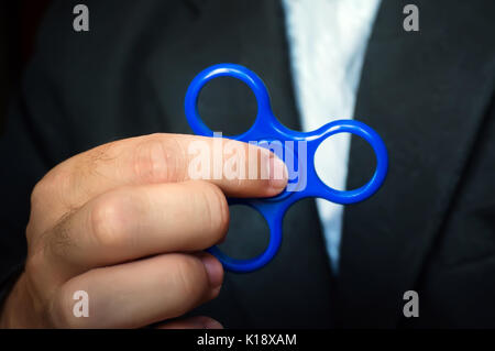 Entspannen, relaxen am Arbeitsplatz, Kopieren, schwarzen Hintergrund. Antistress Spielzeug für nervös. blue Spinner in der Hand eines Büro Stockfoto