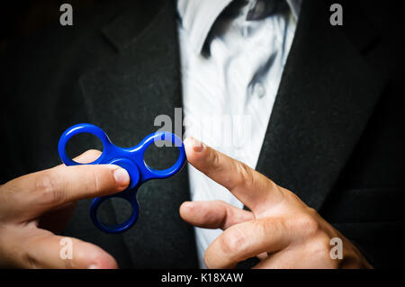 Ein Mann hand Halten einer Hand Spinner oder zappeln Spinner. Leistungsstarke Spinner, Twister für Hände Unterhaltung rotierende Spielzeug. Antistress Spielzeug für einen Geschäftsmann Stockfoto