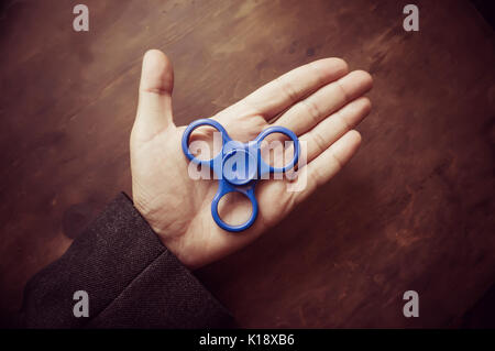 Ein Mann hand Halten einer Hand Spinner oder zappeln Spinner auf dem Hintergrund der hölzernen Tisch. Leistungsstarke Spinner, Twister für Hände Unterhaltung rotierende Spielzeug. Stockfoto