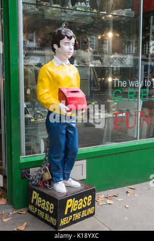 Bitte helfen Sie den Blinden Sammelbox und Statue außerhalb Verhütung von Blindheit der Gesellschaft betrachten wieder Laden auf der Kensington High Street, London, UK Stockfoto