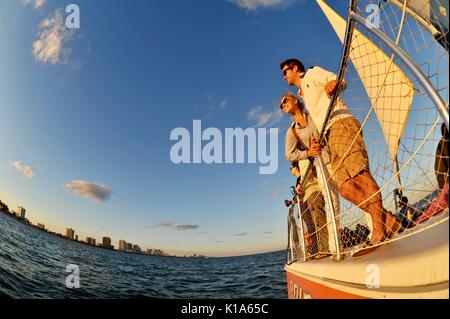 Attraktives junges Paar auf einem Katamaran-Segelboot während einer Bootstour bei Sonnenuntergang auf dem Atlantik außerhalb von ft. Lauderdale, Florida, USA, mit Fischaugenlinse aufgenommen. Stockfoto
