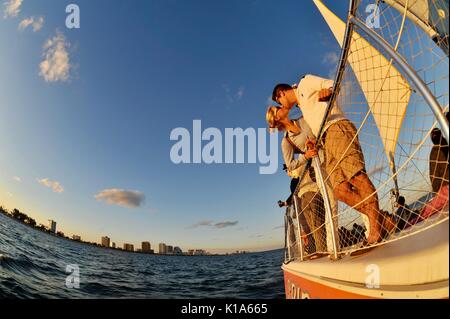 Attraktives junges Paar auf einem Katamaran-Segelboot während einer Bootstour bei Sonnenuntergang auf dem Atlantik außerhalb von ft. Lauderdale, Florida, USA, mit Fischaugenlinse aufgenommen. Stockfoto