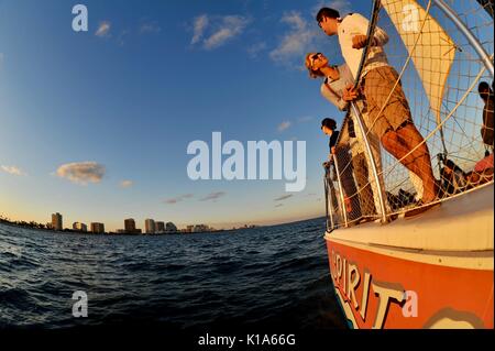 Attraktives junges Paar auf einem Katamaran-Segelboot während einer Bootstour bei Sonnenuntergang auf dem Atlantik außerhalb von ft. Lauderdale, Florida, USA, mit Fischaugenlinse aufgenommen. Stockfoto