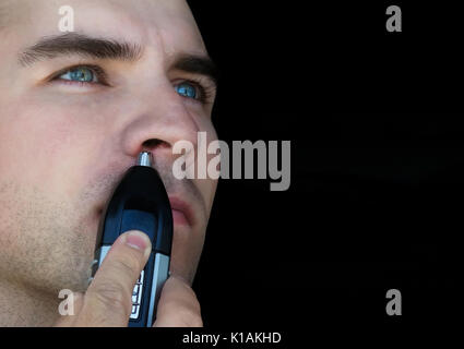 Reinigen Sie die Haare in der Nase - Junge glatzköpfige Mann bürsten Haare in der Nase durch Trimer schwarz isoliert Stockfoto