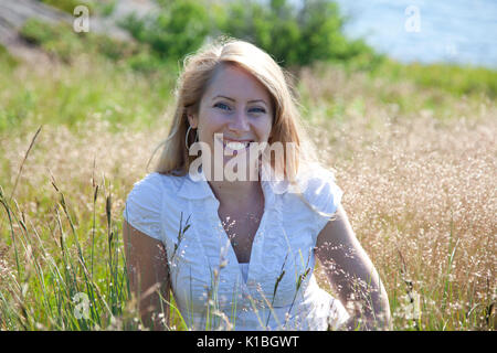Portrait von Glücklich lächelnde junge blonde Frau, draußen in der Wiese. Stockfoto