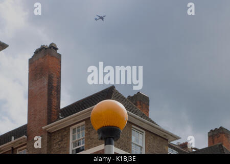 Ein Flugzeug fliegt hoch über Gebäude und einen Zebrastreifen Belisha Beacon, London, England Stockfoto