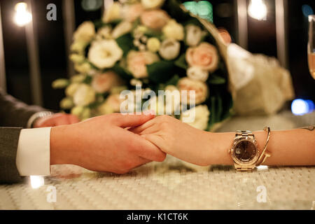 Man macht Frau Heiratsantrag am Tisch im Restaurant und hielt ihre Hand. Es Blumenstrauß aus Rosen im Hintergrund. Stockfoto