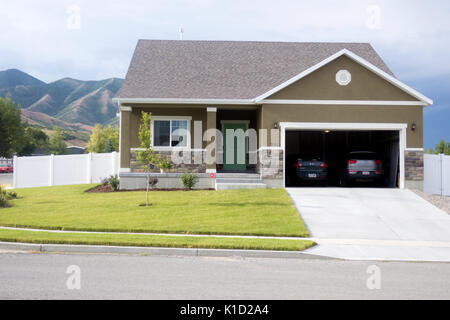 Ein einstöckiges Ranch Haus mit zwei Autos in der Garage auf einer schönen Straße. Stockfoto