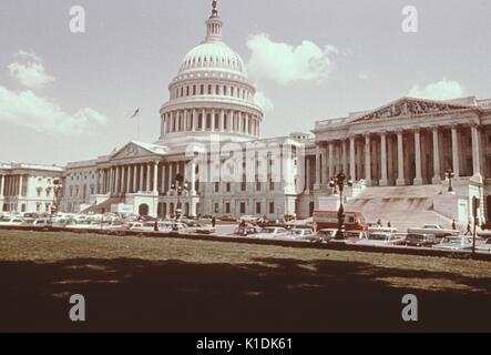 Seite winkel Blick auf die Westfassade des United States Capitol, mit Autos im vorderen Parkplatz geparkt, und mehrere Touristen wandern, Rasen im Vordergrund, Washington, DC, 1966. Stockfoto