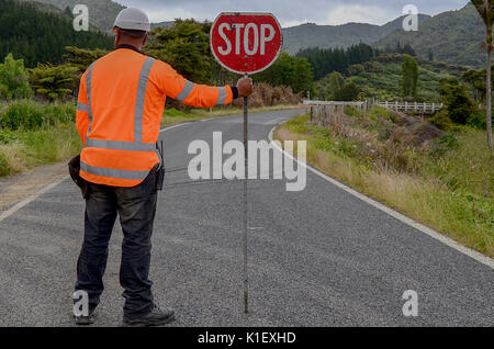 Mann mit STOP-Schild. Mann im roten Mantel über die ländliche Straße. Stockfoto